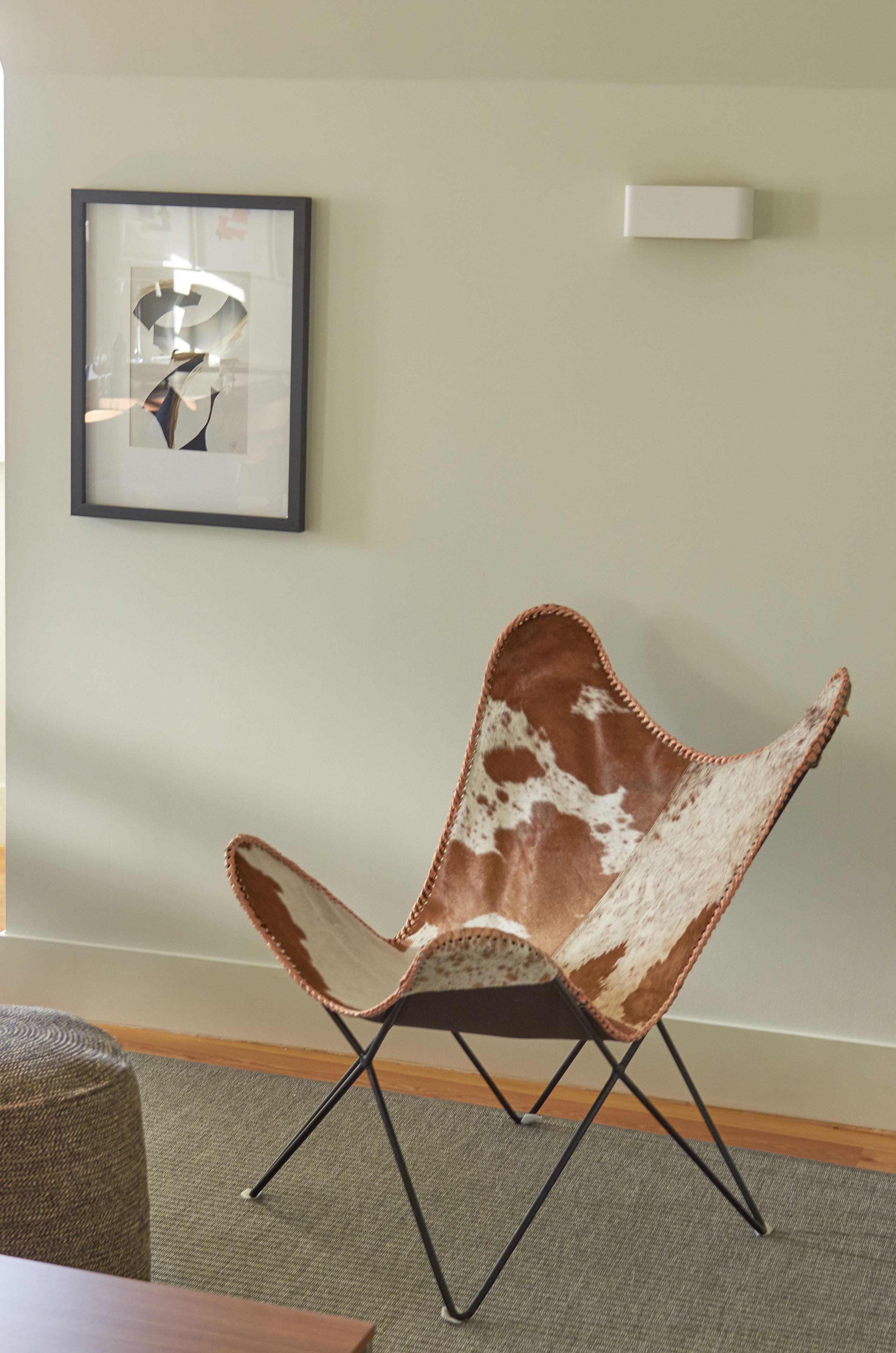 A chair with a unique design, a framed artwork on the wall, and a thermostat.