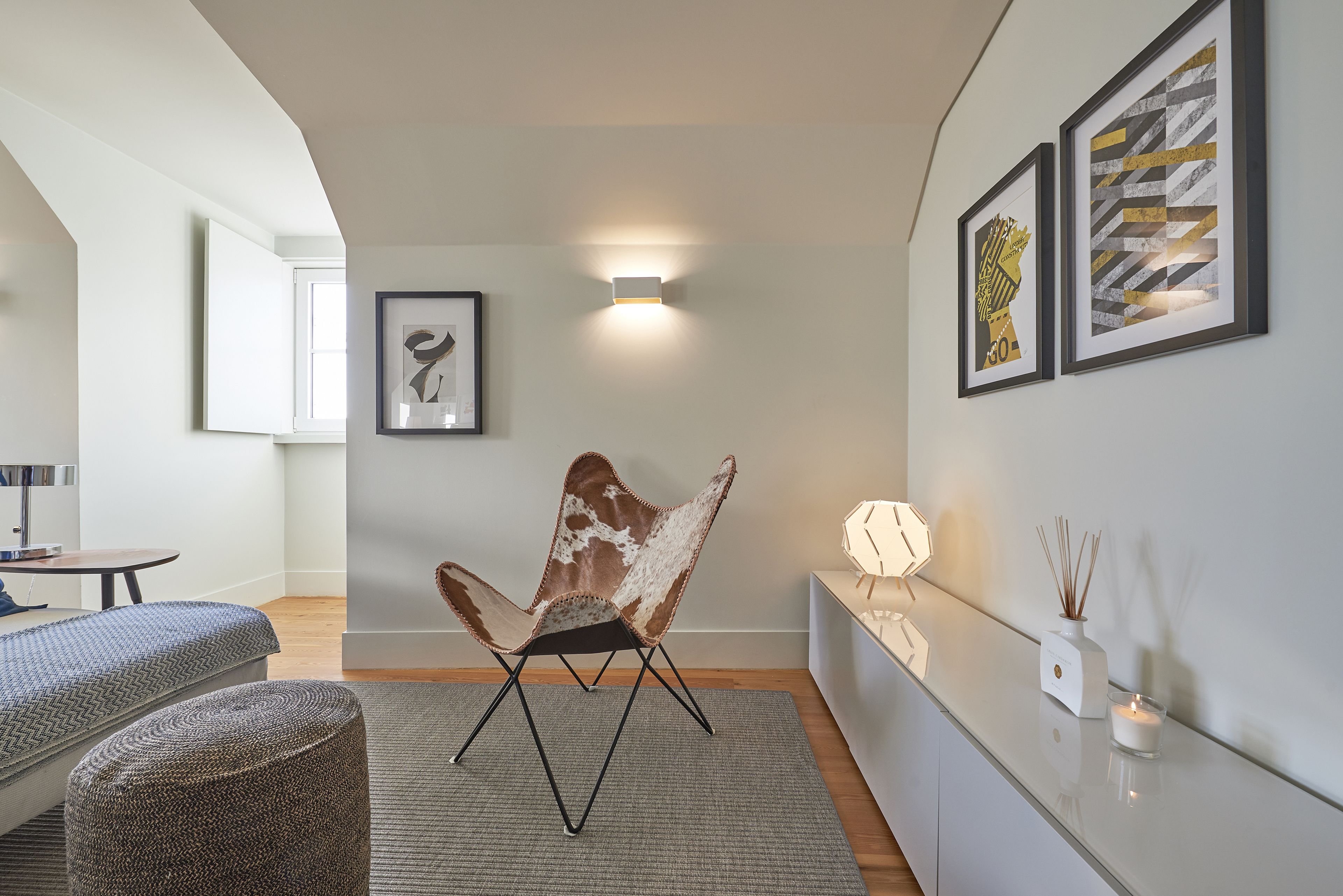 Un salon moderne avec un fauteuil original, une petite table et un canapé. Des œuvres d’art encadrées ornent le mur, ainsi qu’un luminaire fixé au mur.