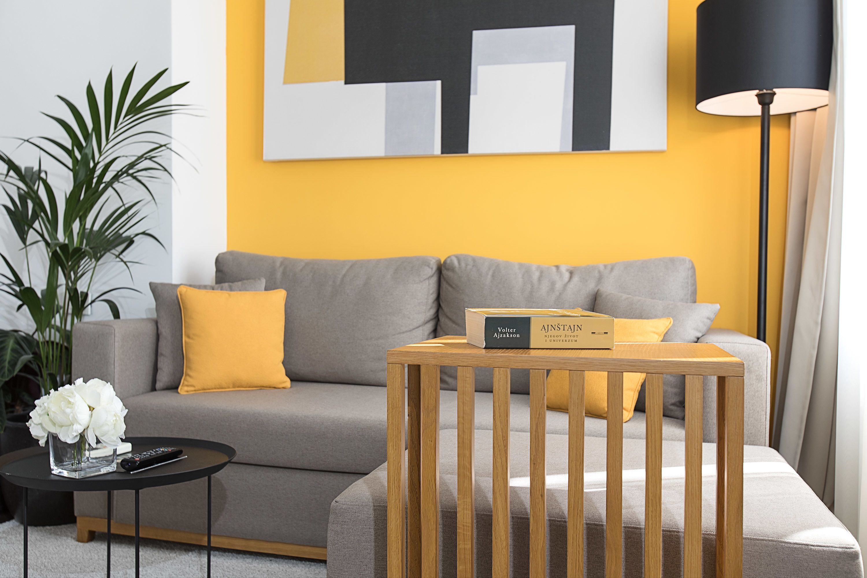A modern living room with a grey sofa, a wooden side table, and a yellow wall.