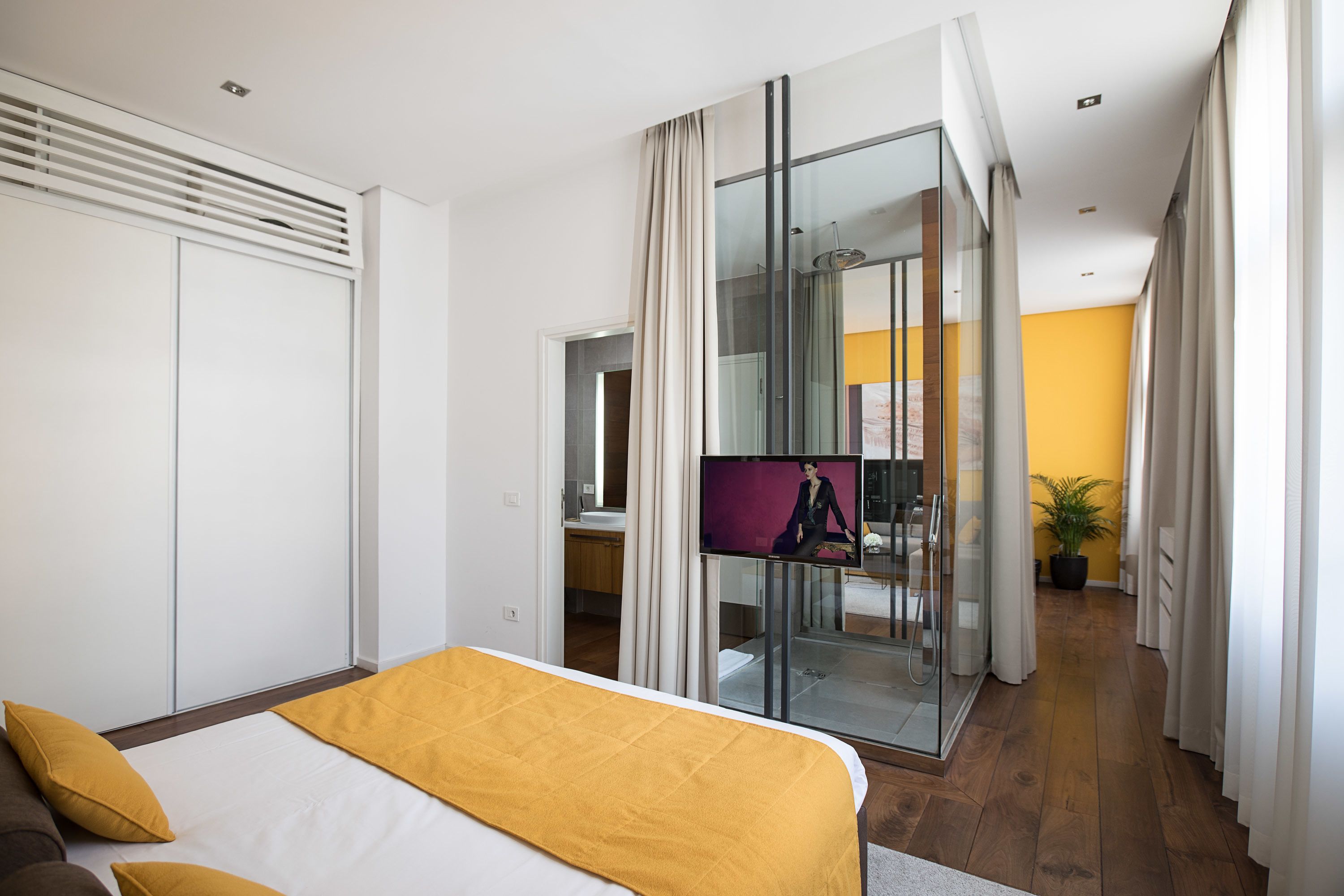 A modern hotel room with a bed, a glass shower enclosure, a bathroom, and a view of the hallway.