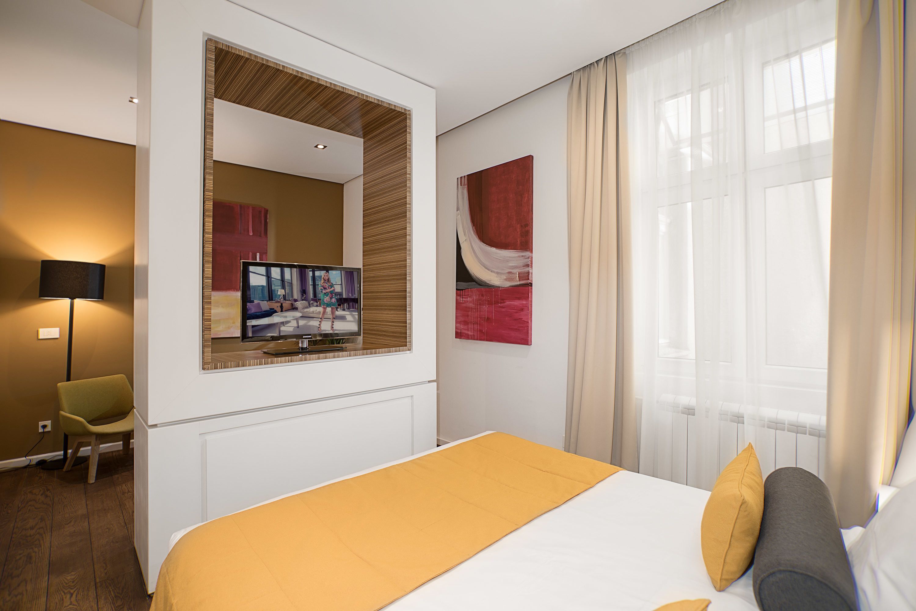 A hotel room with a bed, a television, a chair, and artwork on the walls.