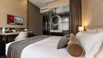 A modern hotel room with a large bed, a desk with a chair, a television, and a circular light fixture.