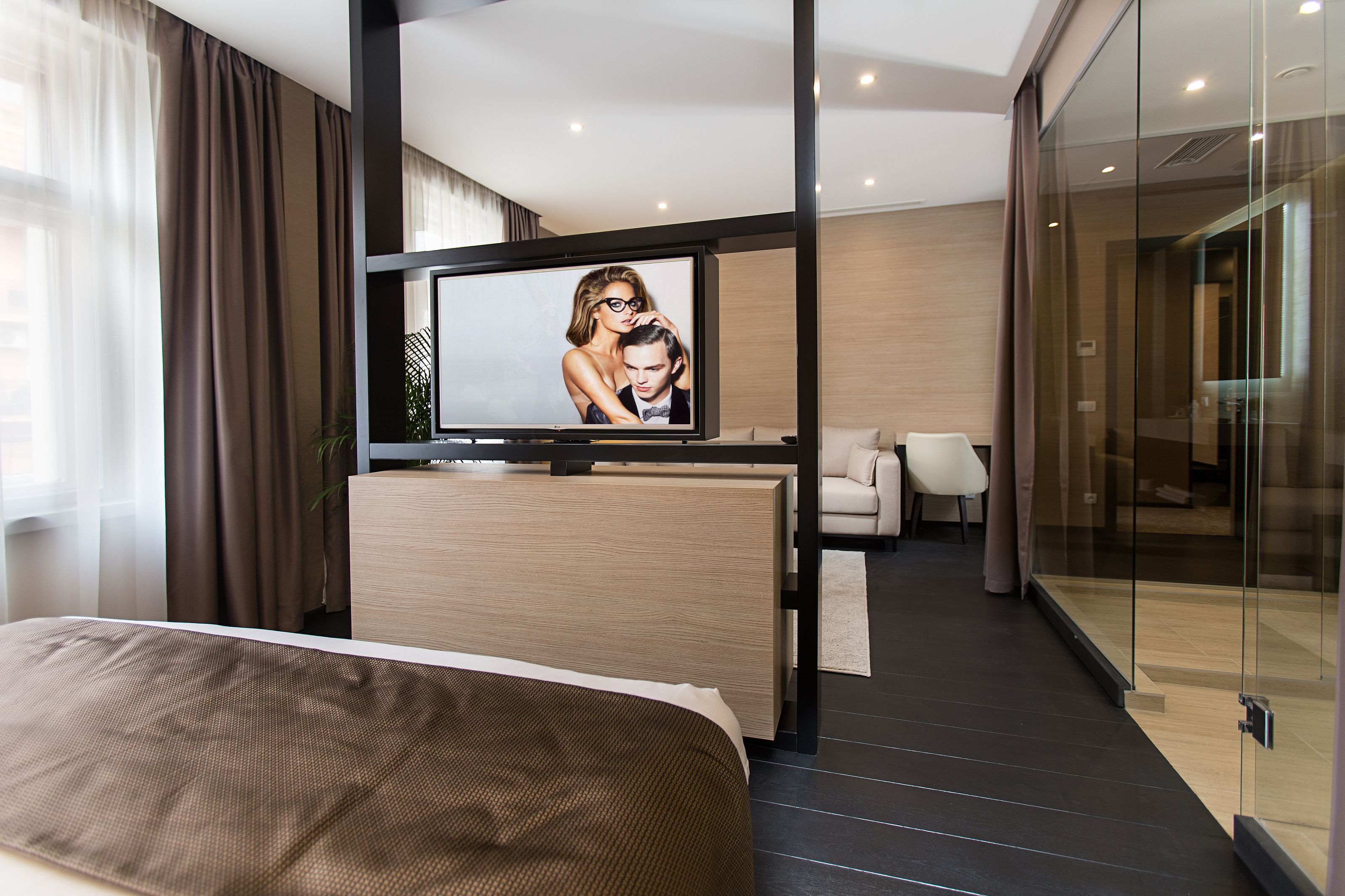 A modern hotel room with a bed, a television, a sofa, and a glass partition.