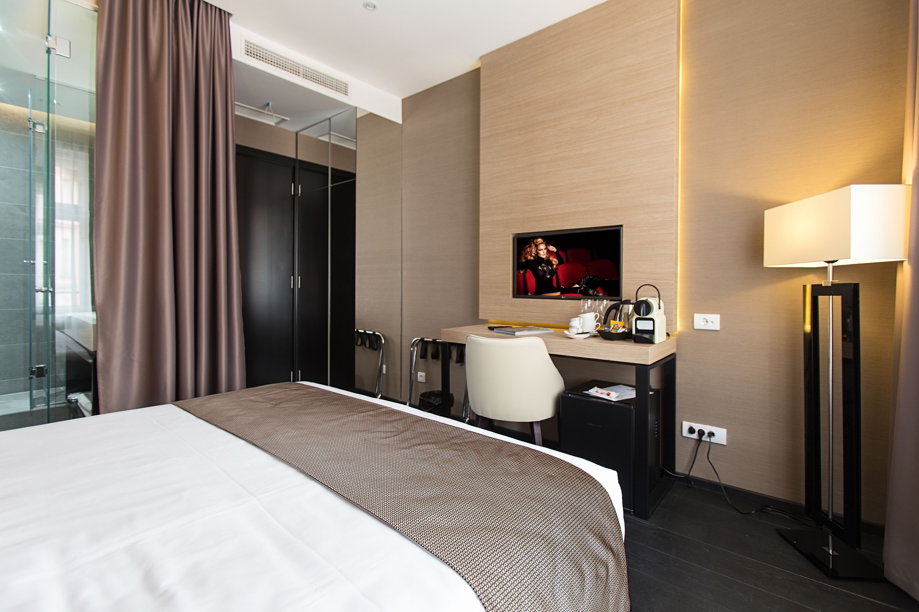 Une chambre d’hôtel moderne dotée d’un grand lit, d’un bureau avec un ordinateur, d’une télévision et d’une douche en verre.