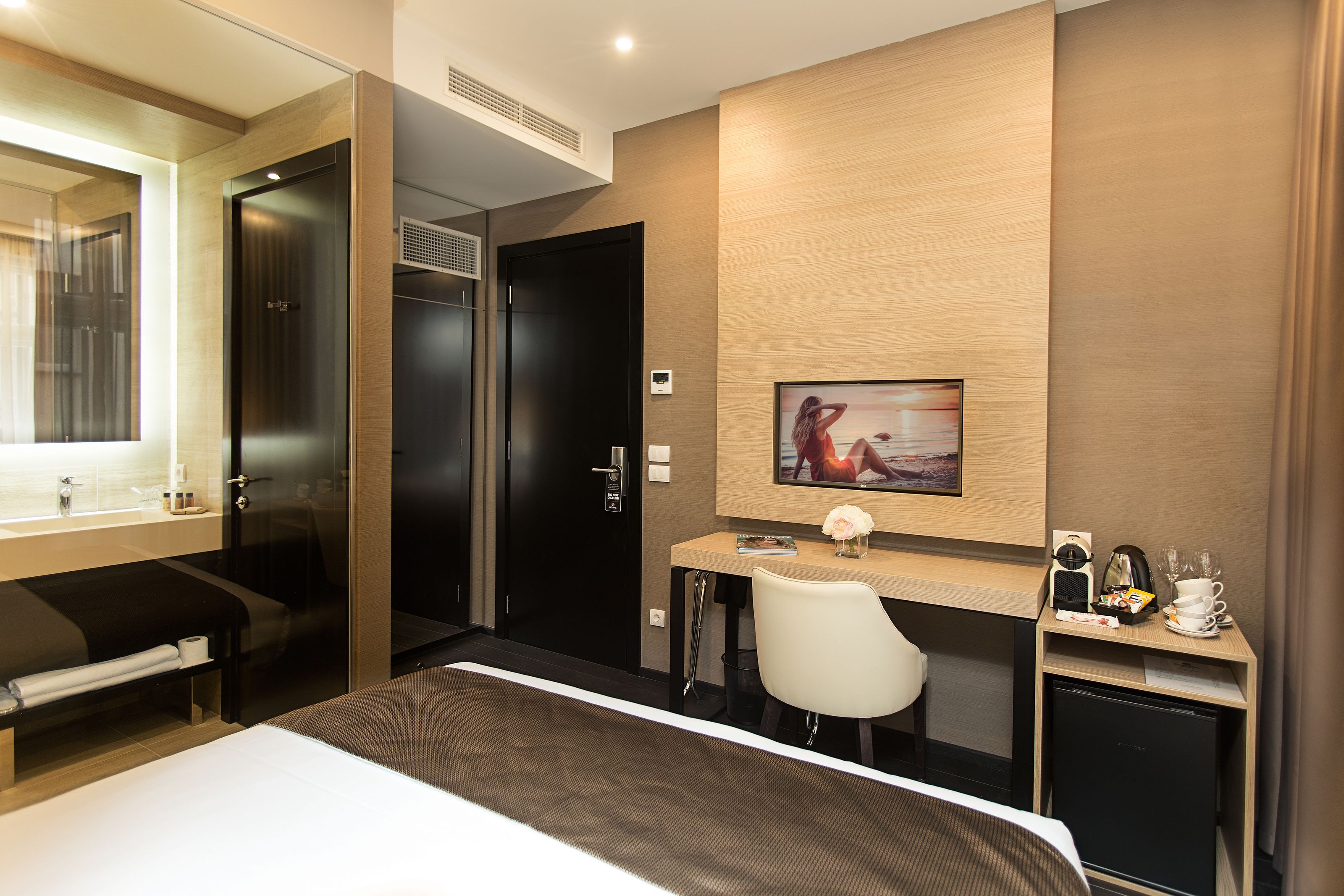 A modern hotel room with a bed, a desk, a chair, and a small kitchenette.