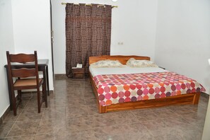 Un dormitorio con una cama de madera, una silla, un escritorio y una cortina estampada.