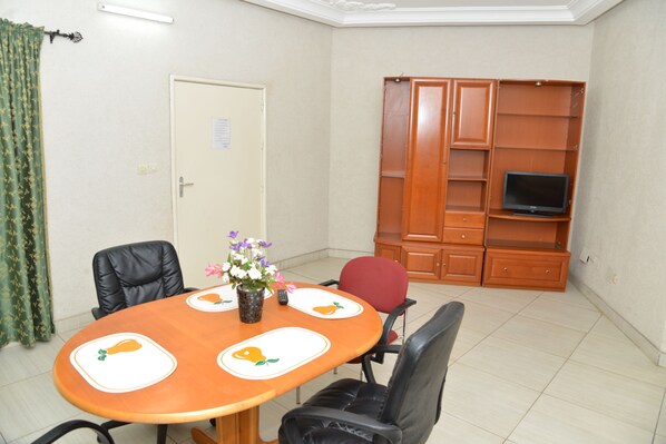A conference room with a wooden table, black chairs, a vase with flowers, and a television on a wooden cabinet.