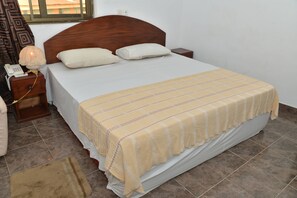 Una cama bien hecha con un edredón a rayas, una lámpara de noche y un teléfono sobre una mesita de madera.