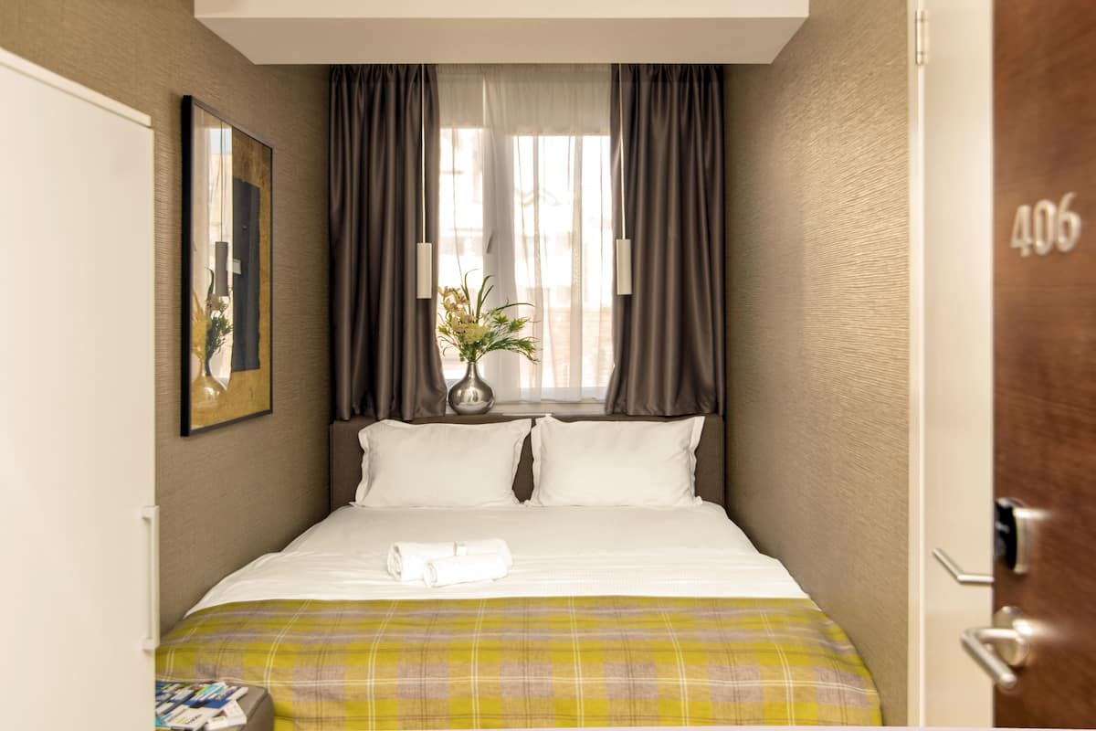 Ett hotellrum med en säng, gardiner, ett fönster och en dörr.