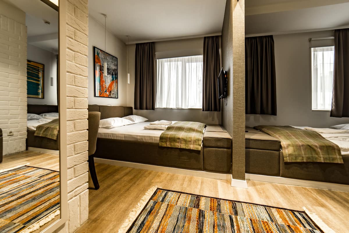 Ett hotellrum med en tegelvägg, ett stort fönster med gardiner, en säng, en soffa och en tv.