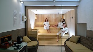 A modern spa room with wooden benches and a glass partition. There are two people in white robes, one sitting and one standing. - Hotel Belgrade Inn (Belgrade)