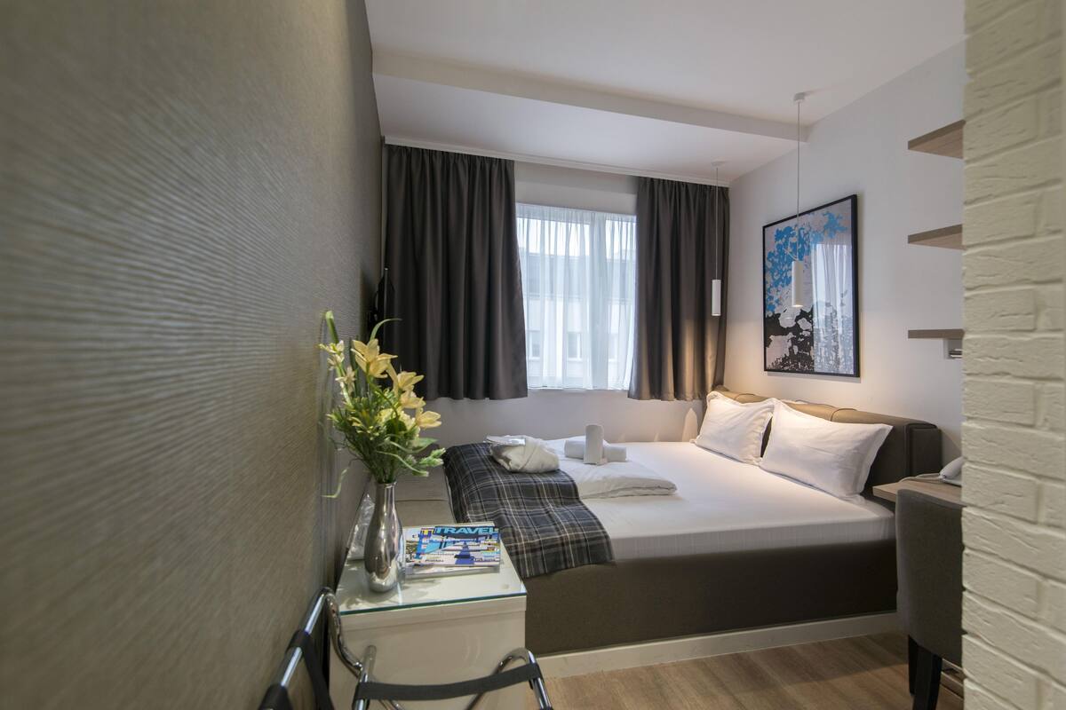 Ett modernt hotellrum med en säng, ett nattduksbord och ett fönster med gardiner.