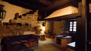 Une pièce chaleureuse avec un mur en pierre, un banc en bois, un banc rembourré, une petite table avec une lampe et une fenêtre donnant sur un beau paysage.