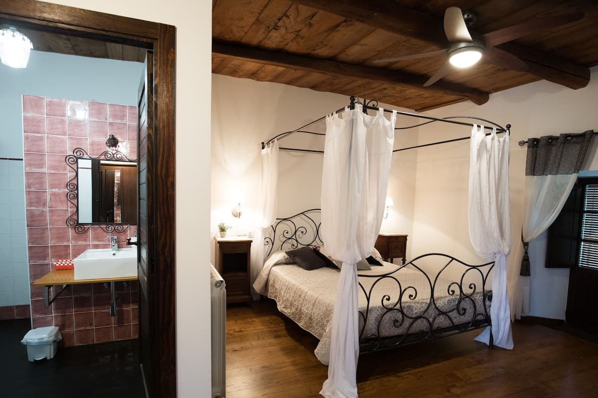 Un dormitori amb un llit amb cortines, sostre de fusta i un bany amb rajola, un lavabo i un mirall.