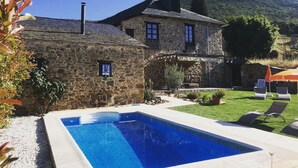Une maison en pierre avec une piscine, entourée d’une pelouse bien entretenue et d’une colline en arrière-plan.