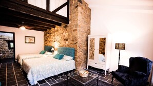 Une chambre avec un mur en pierre, un lit avec une tête de lit bleue, une table basse noire, une chaise et une lampe.