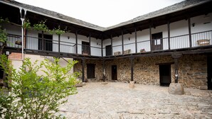 Une cour dallée de pierres, un balcon en bois et un bâtiment en pierre doté de nombreuses portes et fenêtres.