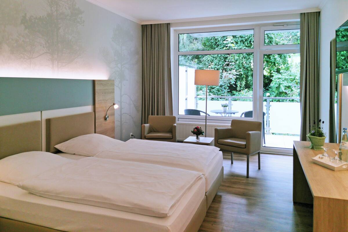 Hotellihuone, jossa on kaksi sänkyä, työpöytä, tuoli ja näkymä ulos.
