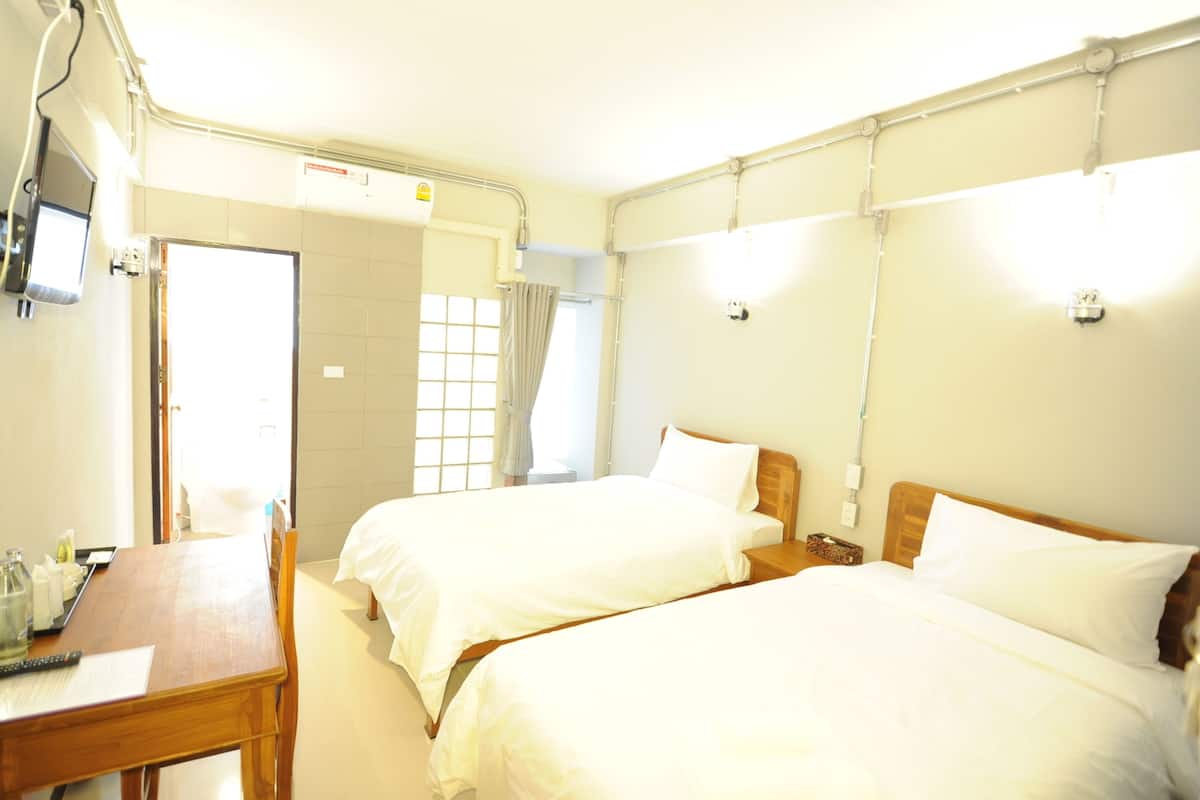 A hotel room with two beds, a wooden desk, and a window with curtains.