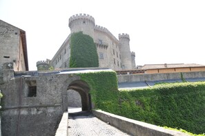 Un château historique en pierre, doté d’une tour centrale, d’une entrée en arc de cercle et d’un mur d’enceinte agrémenté de verdure.