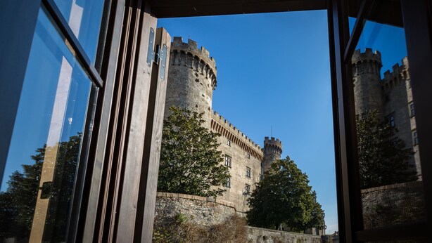 Un castillo con muro de piedra y una torre, visto a través de una ventana con barrotes.