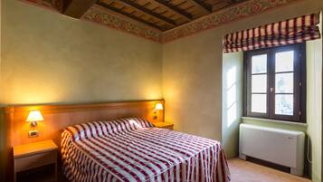 Una camera d'albergo con un letto, due lampade ai comodini, una finestra con tenda a righe e un termosifone.
