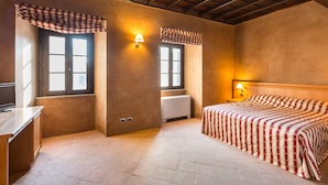 Un dormitorio con cama, dos ventanas con cortinas, una lámpara de noche y un radiador.
