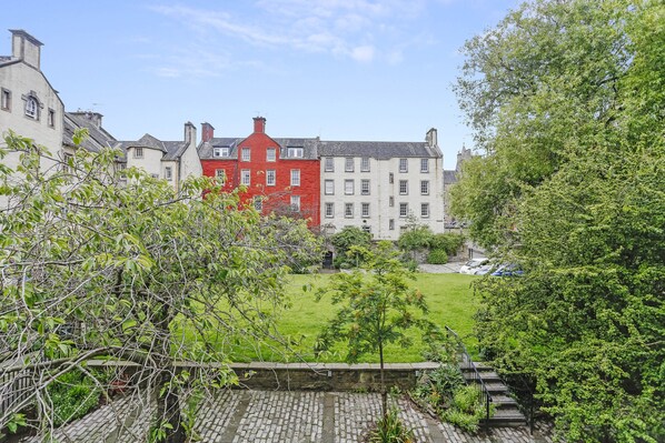 A courtyard with a brick pathway, surrounded by buildings with varied architectural styles, including a prominent red building. - Edinburgh Landmarks Apartments (Edinburgh)