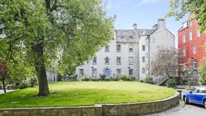 A historic building with a stone facade, a well-maintained lawn, and a blue car parked in front. - Edinburgh Landmarks Apartments (Edinburgh)