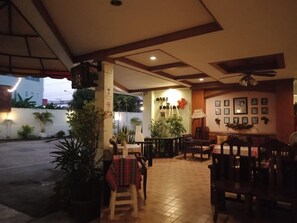 An indoor dining area with tables and chairs, potted plants, and a wall with framed pictures. - Casa Holiday Hotel (Phitsanulok)