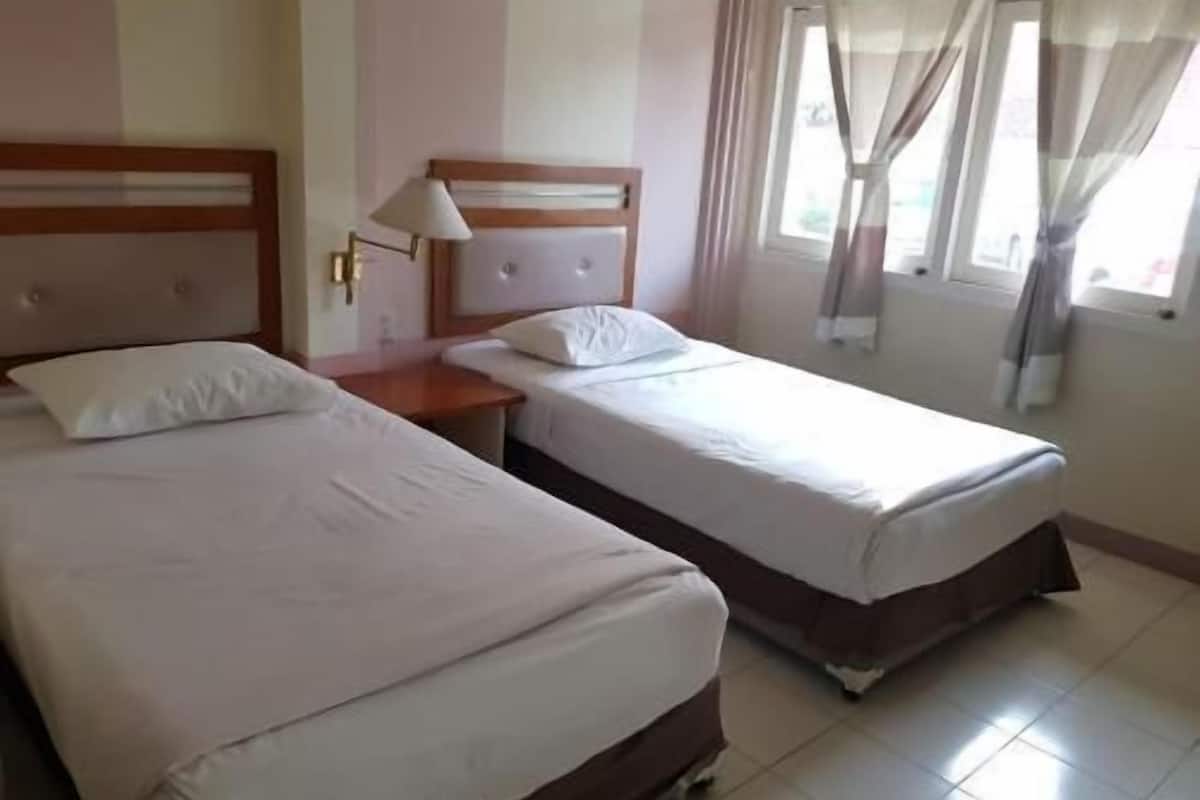 Une chambre d’hôtel avec deux lits, une table de chevet, une lampe et une fenêtre avec des rideaux.