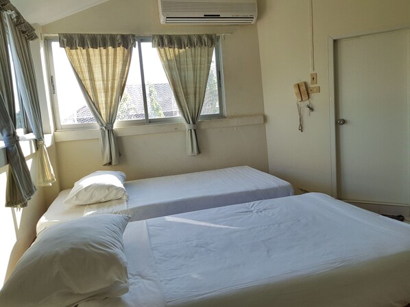 A room with two single beds, a window with curtains, an air conditioning unit, a telephone, and a door. - Casa Holiday Hotel (Phitsanulok)