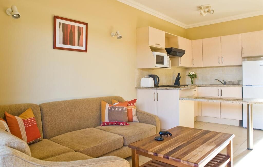 Een woonkamer met een bank, een salontafel en een keuken met kasten en apparatuur.