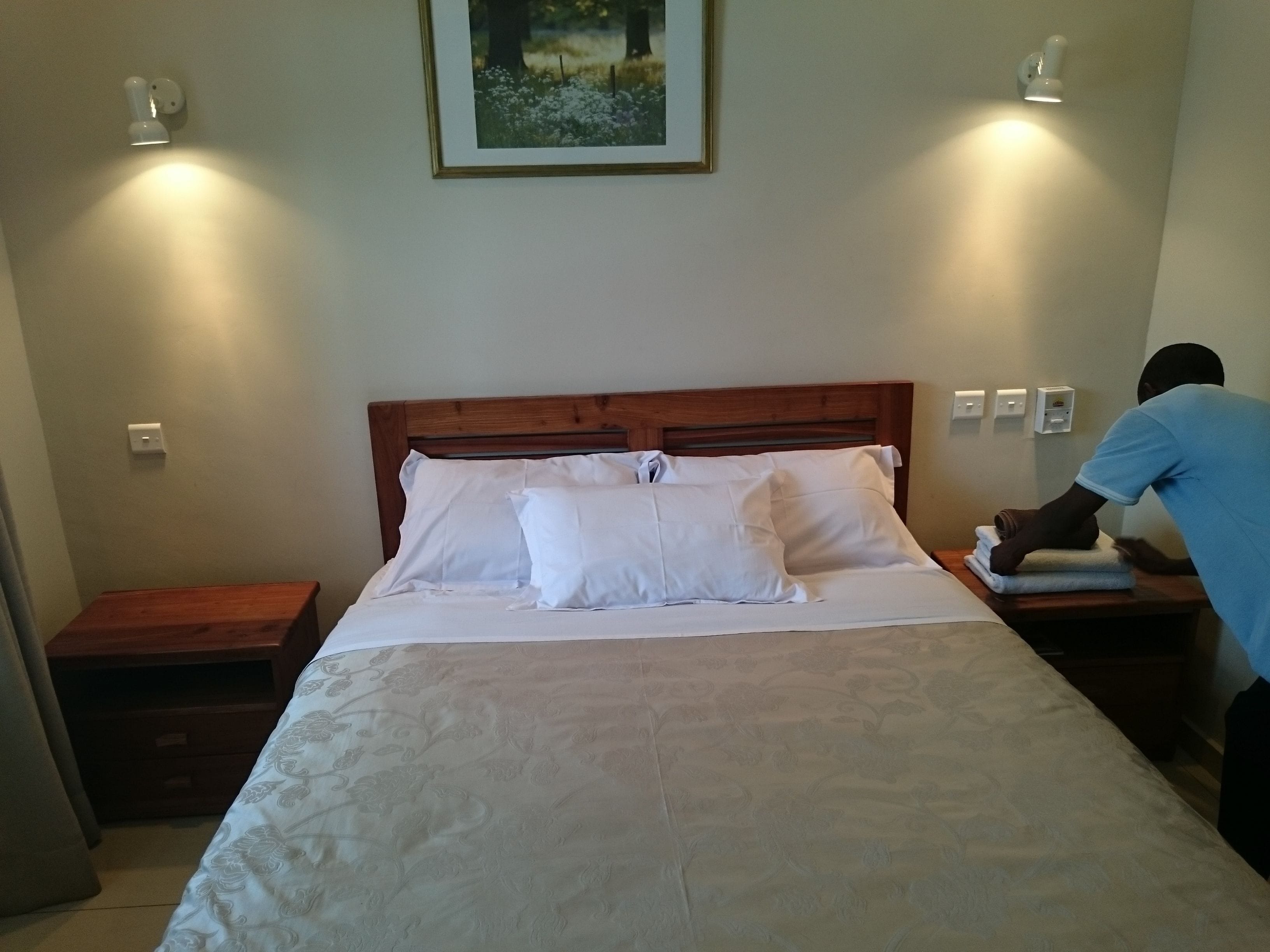 Een keurig opgemaakt bed met witte lakens en een houten hoofdeinde, twee nachtkastjes en een ingelijst beeld aan de muur.