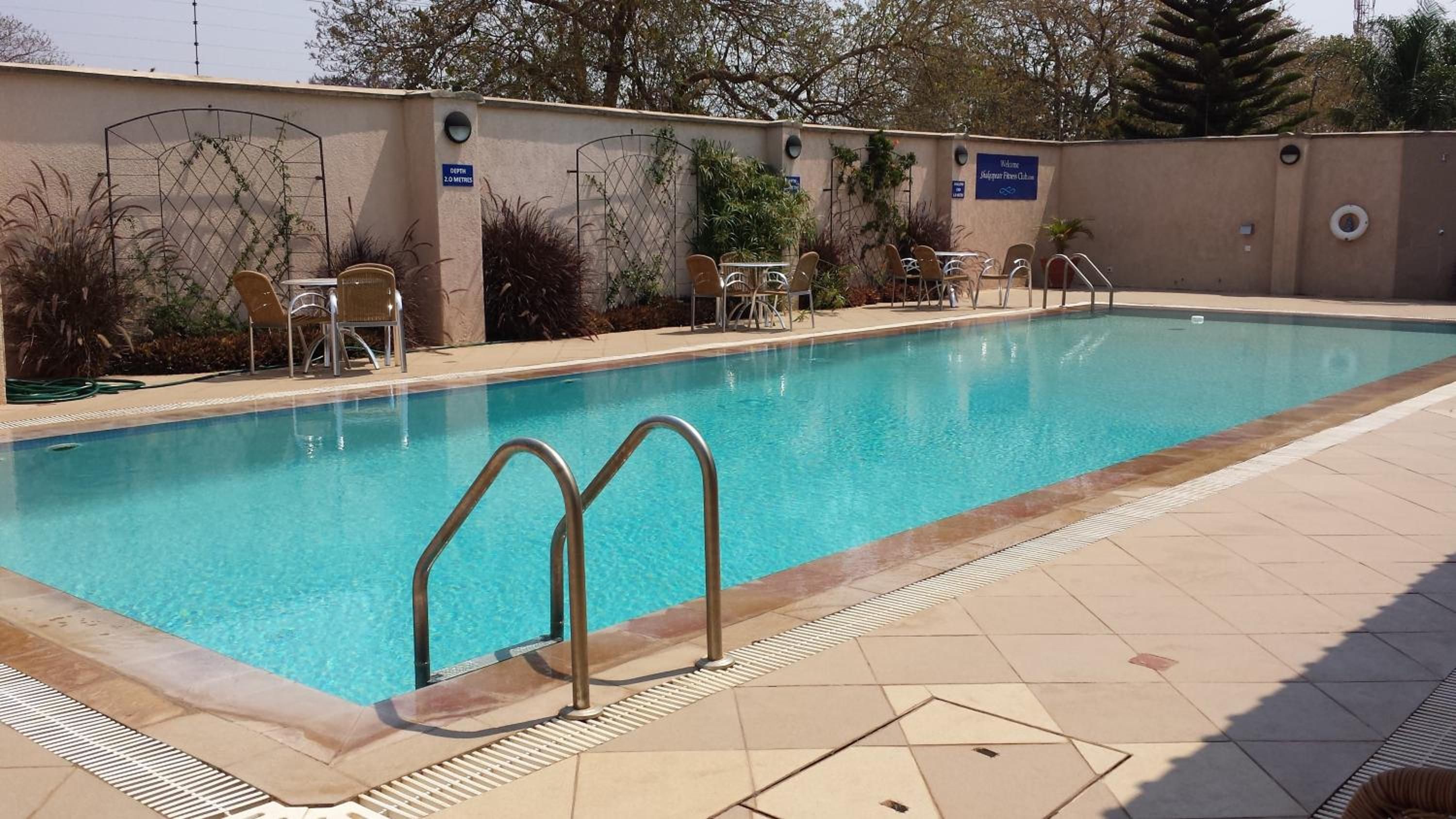 A swimming pool with a metal ladder, surrounded by lounge chairs and a wall with a sign.