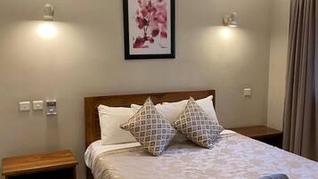 Una cama bien hecha con almohadas estampadas, una obra de arte floral enmarcada en la pared y una toalla enrollada sobre la cama.