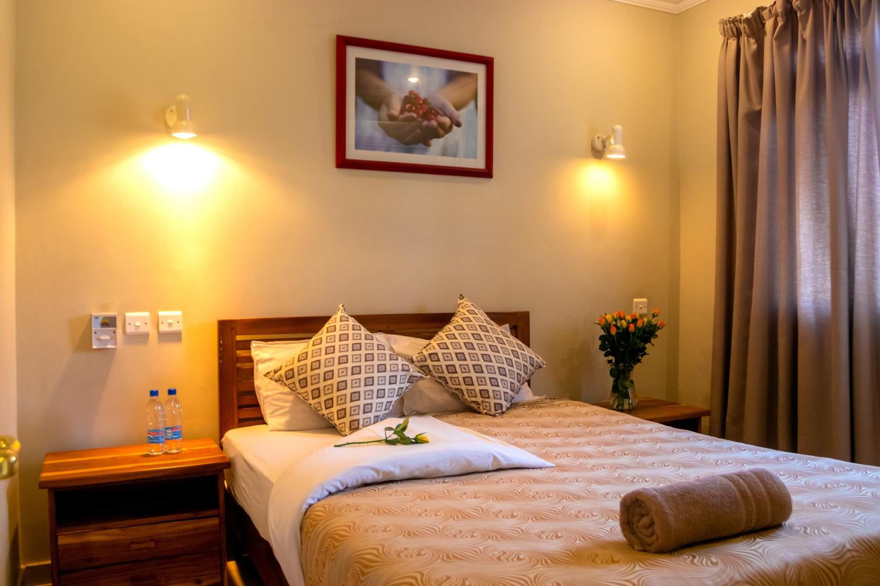 A hotel room with a bed, two bedside tables, a nightstand, a vase with flowers, and a framed picture on the wall.