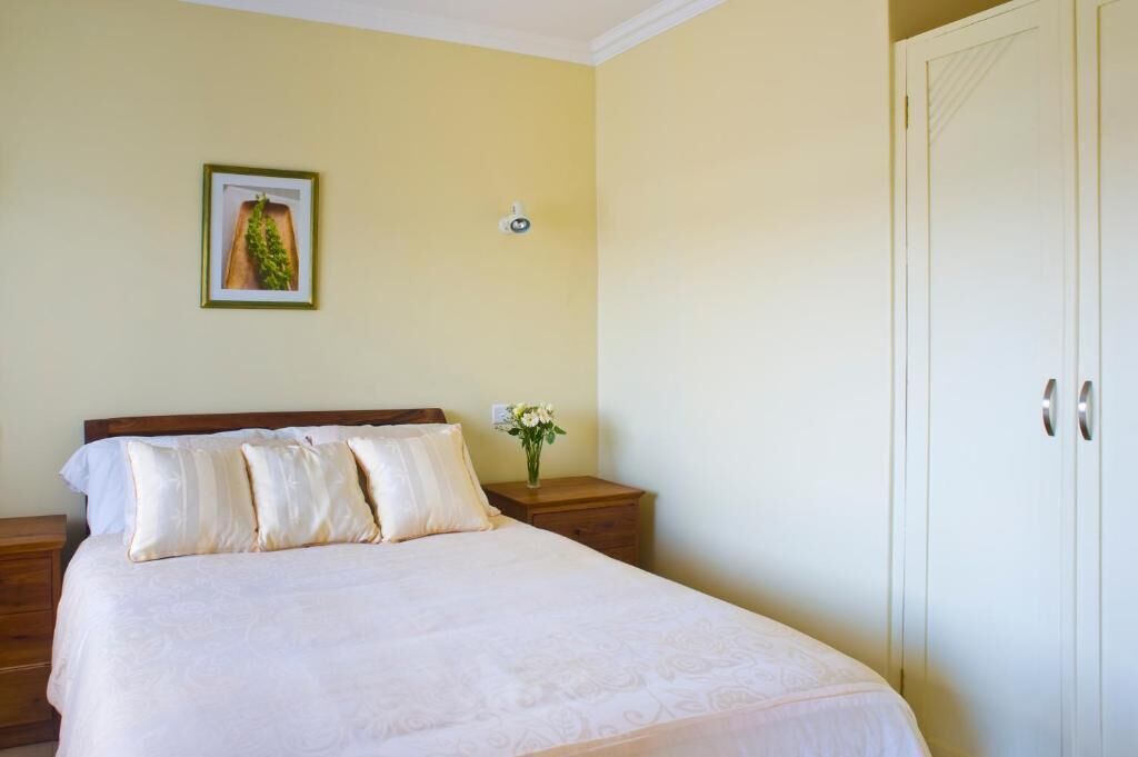 A bedroom with a bed, nightstands, a wall-mounted light, and a door.