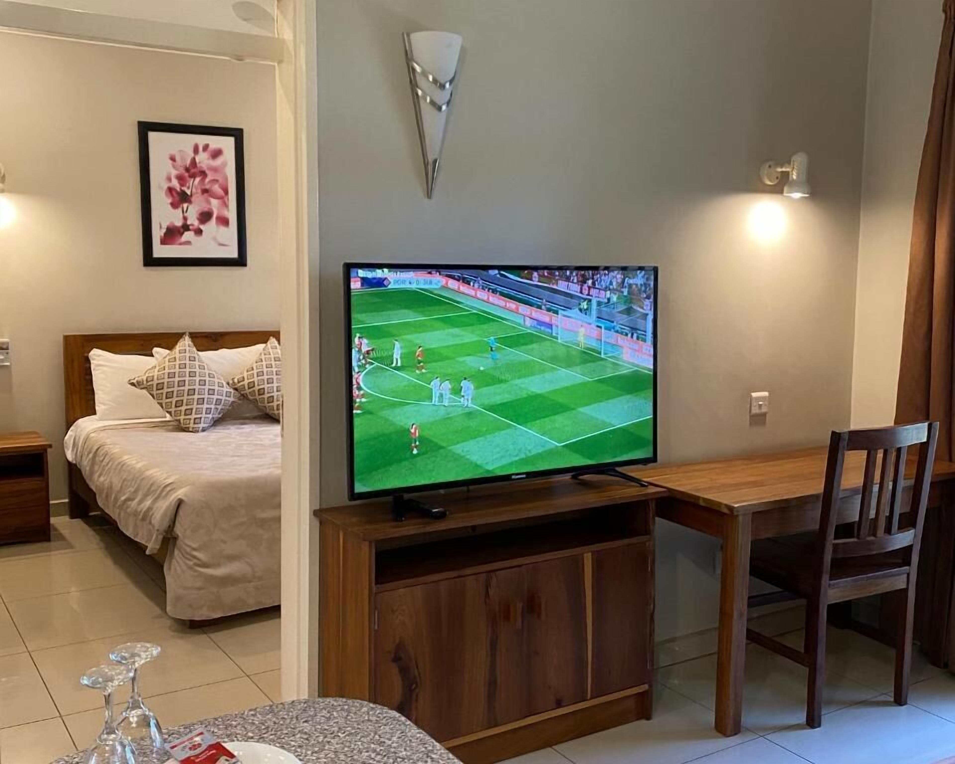 A bedroom with a bed, bedside table, and a television displaying a sports game.