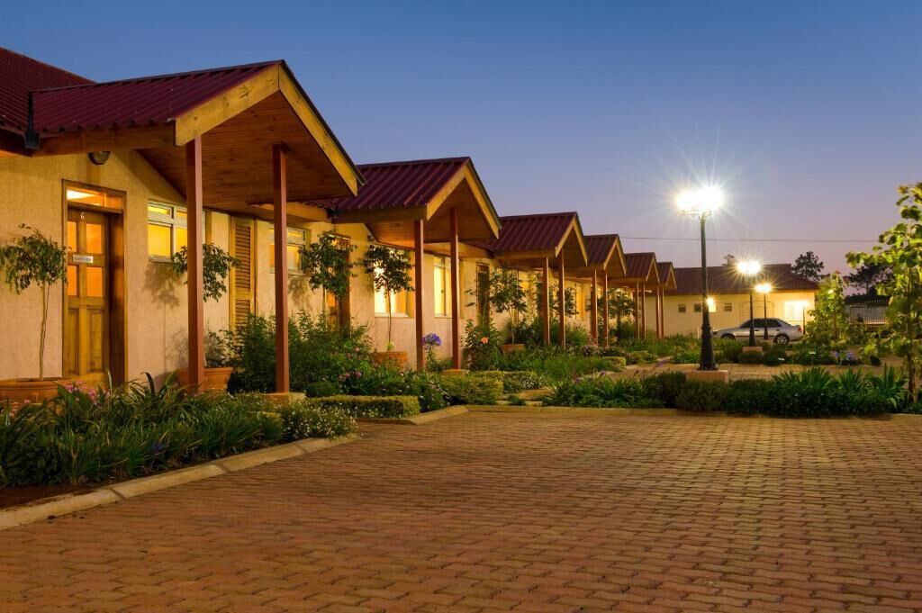 A row of hotel buildings with a paved walkway and greenery in front.