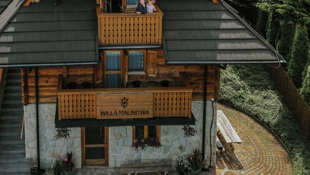 Un chalet in legno con balcone, chiamato "Villa Malinowa", con rivestimento in pietra e cortile lastricato.
