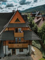 A wooden chalet with a balcony, named "Villa Malinowa," featuring a stone facade and a paved courtyard.