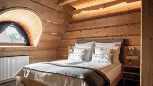 Una camera da letto mansardata accogliente, con travi in legno a vista, un'ampia finestra e un letto con numerosi cuscini e una coperta.