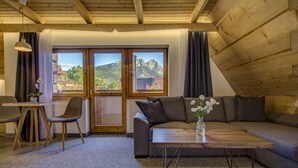 Un accogliente soggiorno con soffitto in legno, un divano grigio, un tavolino in legno e vista sulle montagne attraverso ampie finestre.