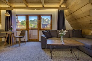 A cozy living room with a wooden ceiling, a gray sofa, a wooden coffee table, and a view of mountains through large windows.