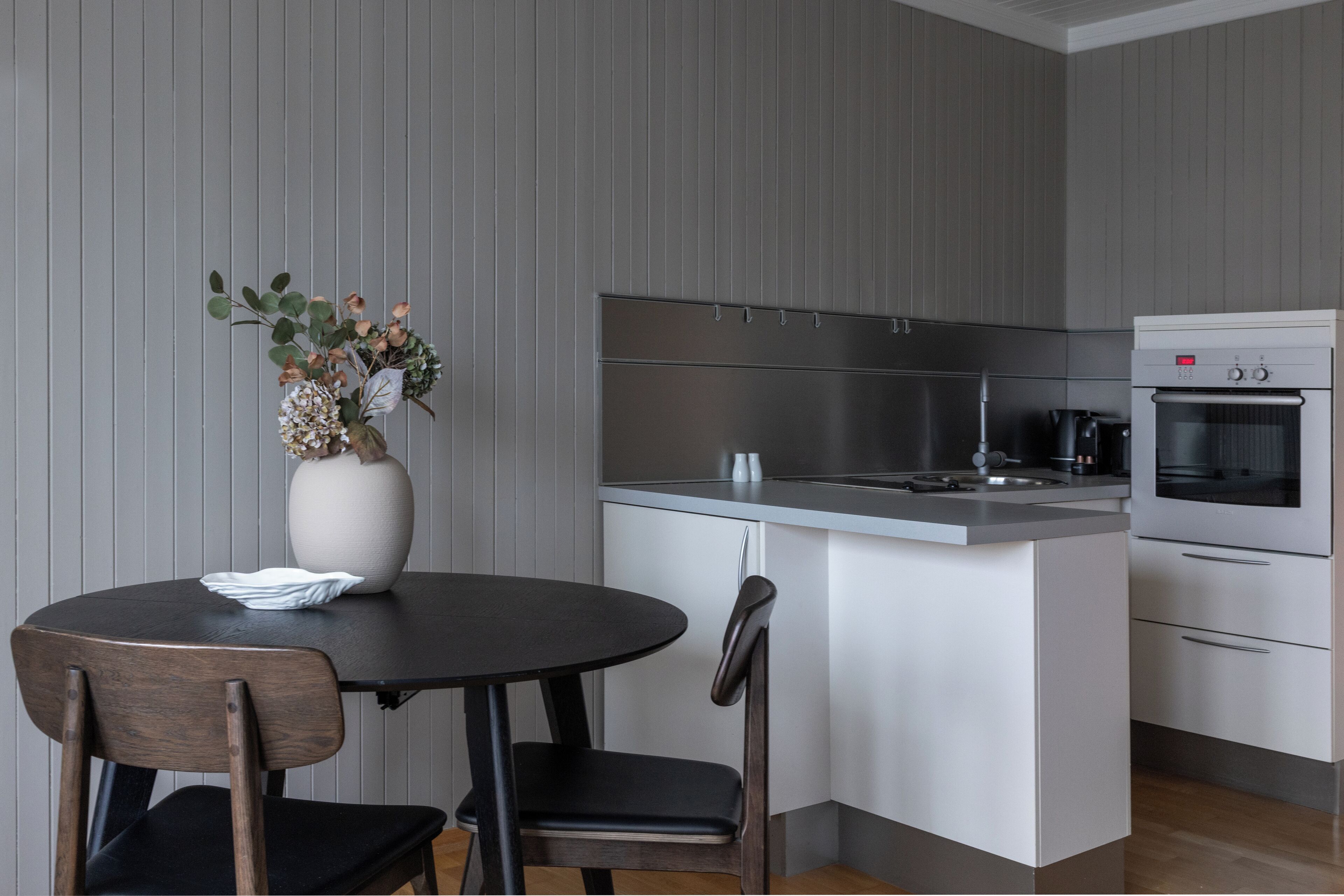 A modern kitchen with a central island, stainless steel appliances, and a dining area with a vase of flowers.