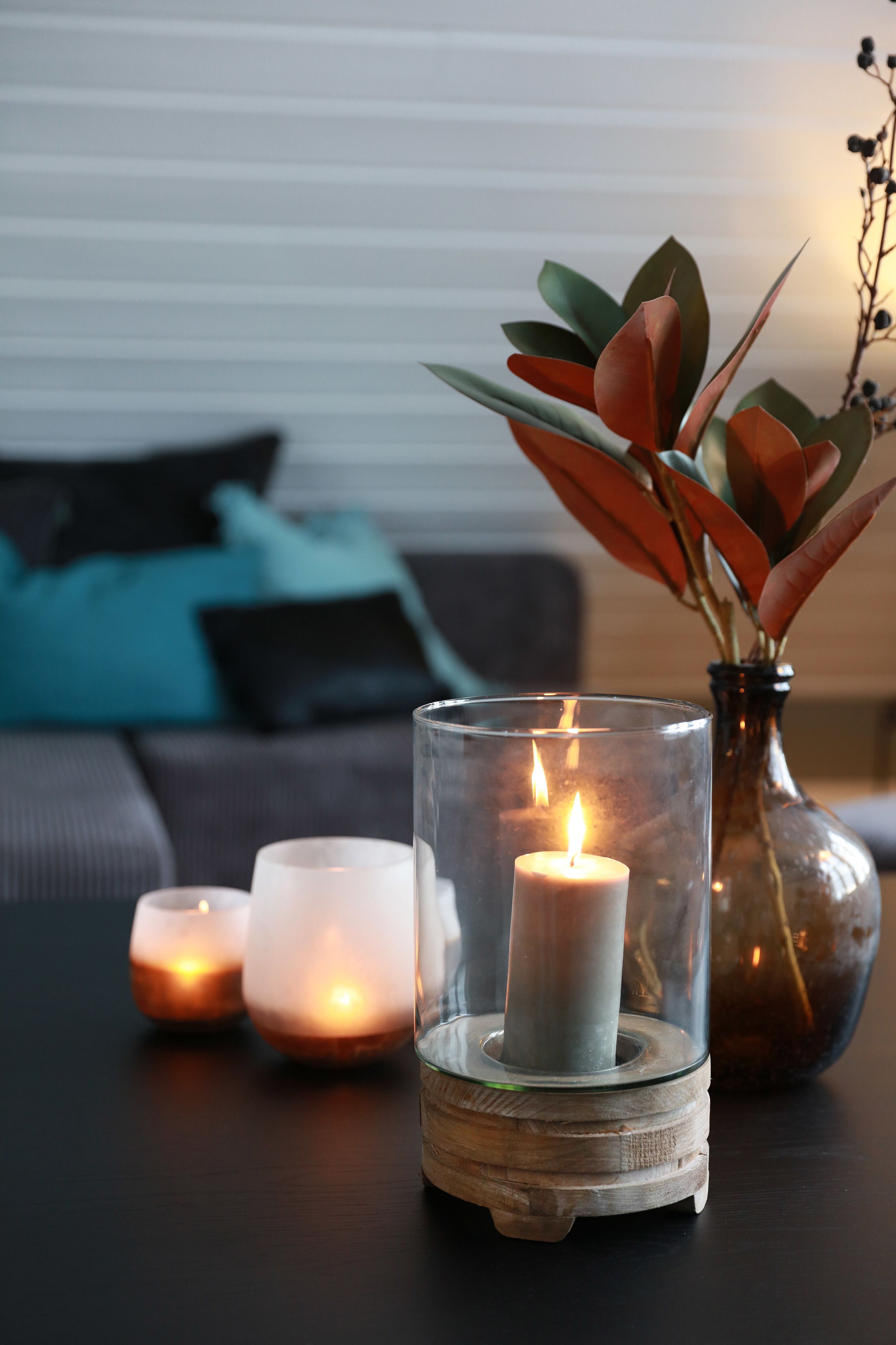 Una mesa con velas y un florero con hojas verdes.