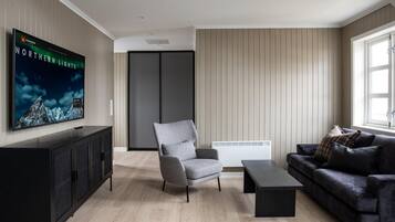 A modern living room with a flat-screen TV, a grey armchair, a black sofa, a coffee table, and a cabinet.