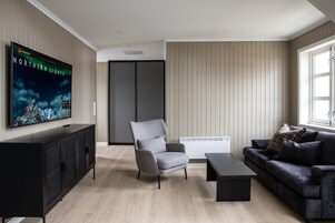 A modern living room with a flat-screen TV, a grey armchair, a black sofa, a coffee table, and a cabinet.