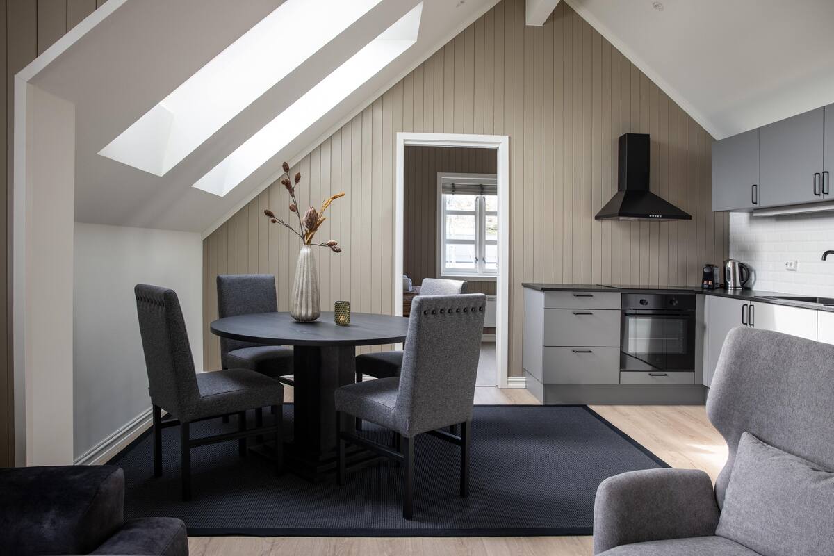 Une cuisine moderne dotée d’une verrière, de meubles de rangement gris et d’un coin repas avec une table ronde et des chaises.